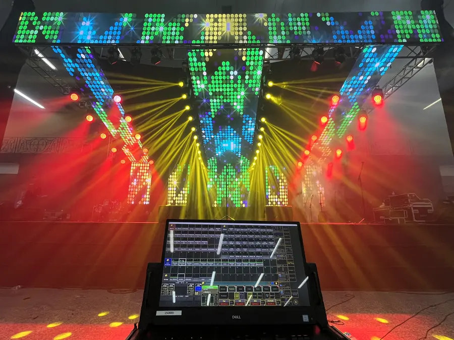 Grande painel de LED em formato de arco no palco, com mesa de controle de iluminação em primeiro plano